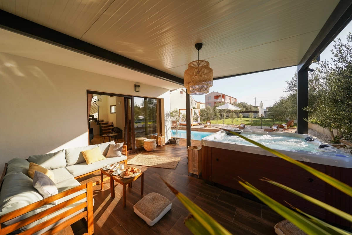 Überdachte Terrasse der Villa Sunčica mit Whirlpool, gemütlichen Sitzmöbeln und Blick auf den Pool und den grünen Garten.