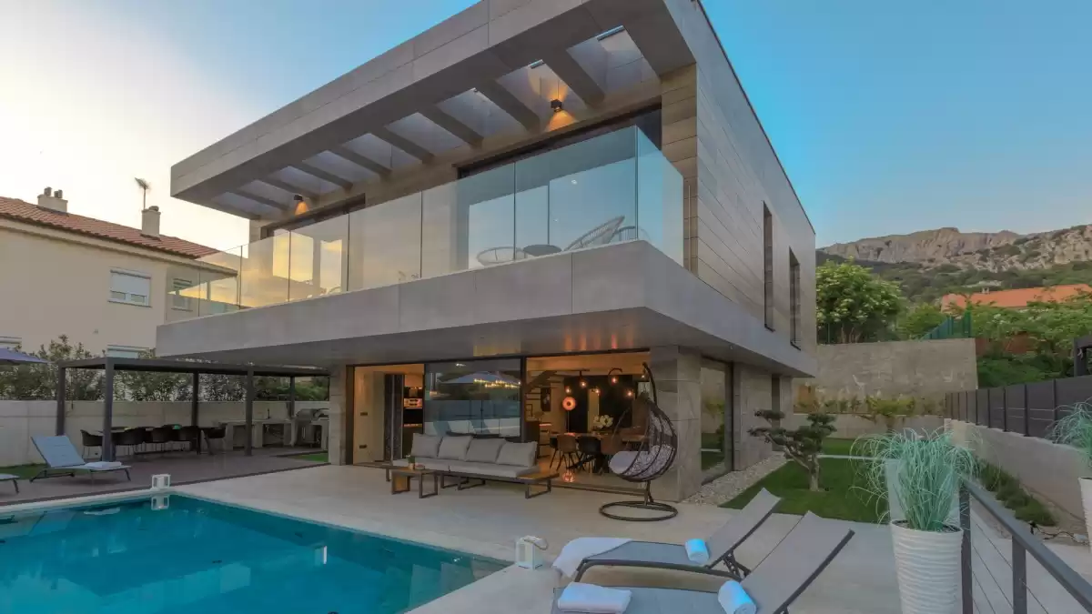 Villa Besca, a modern luxury villa with a private pool, spacious terrace, and glass façade, set against a backdrop of lush greenery and mountain views