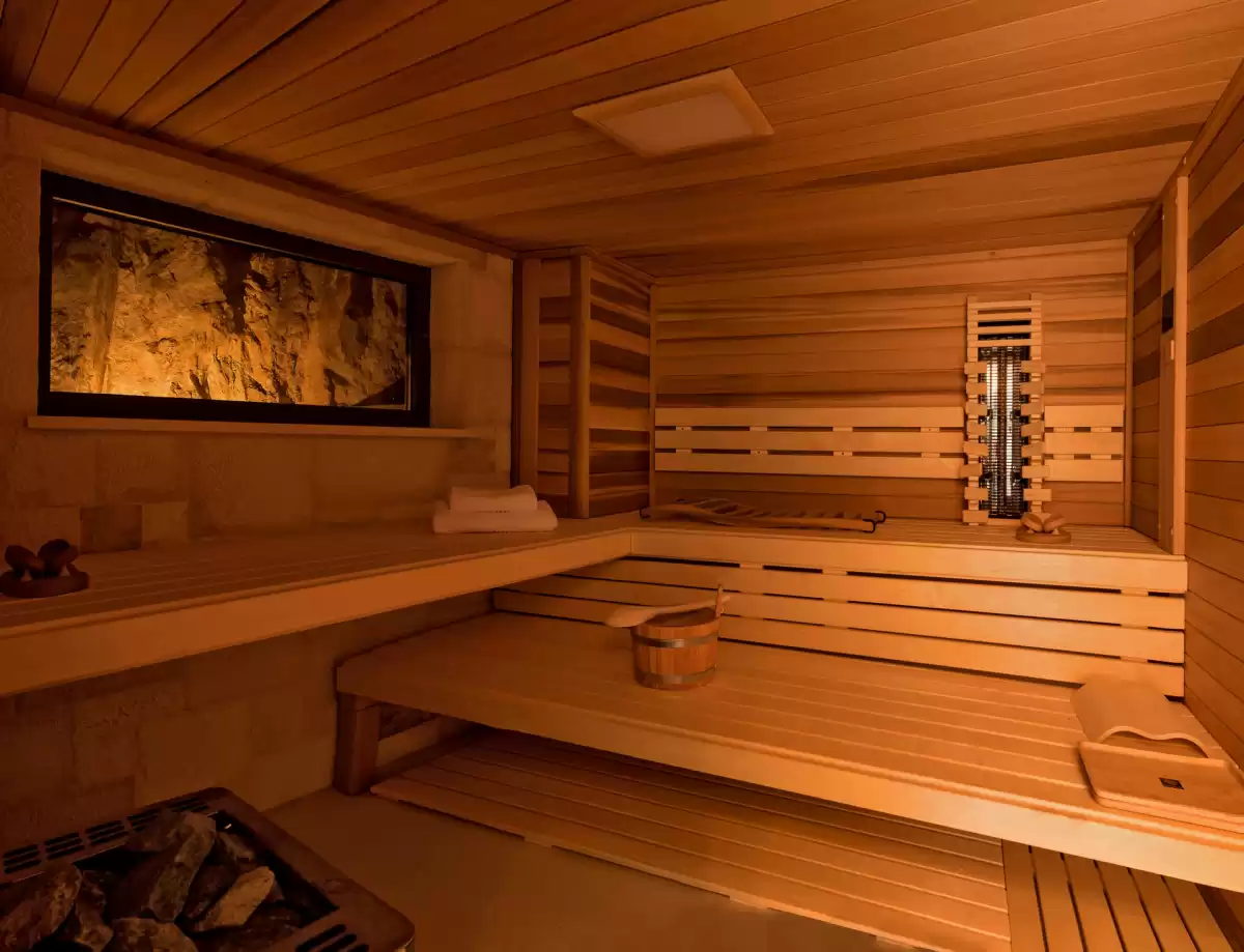 Elegant wooden sauna at Villa Mila on Brač Island, featuring a traditional stone heater and comfortable benches for relaxation. A window opening provides a unique view of the illuminated rock, creating a cozy ambiance for a complete wellness experience.