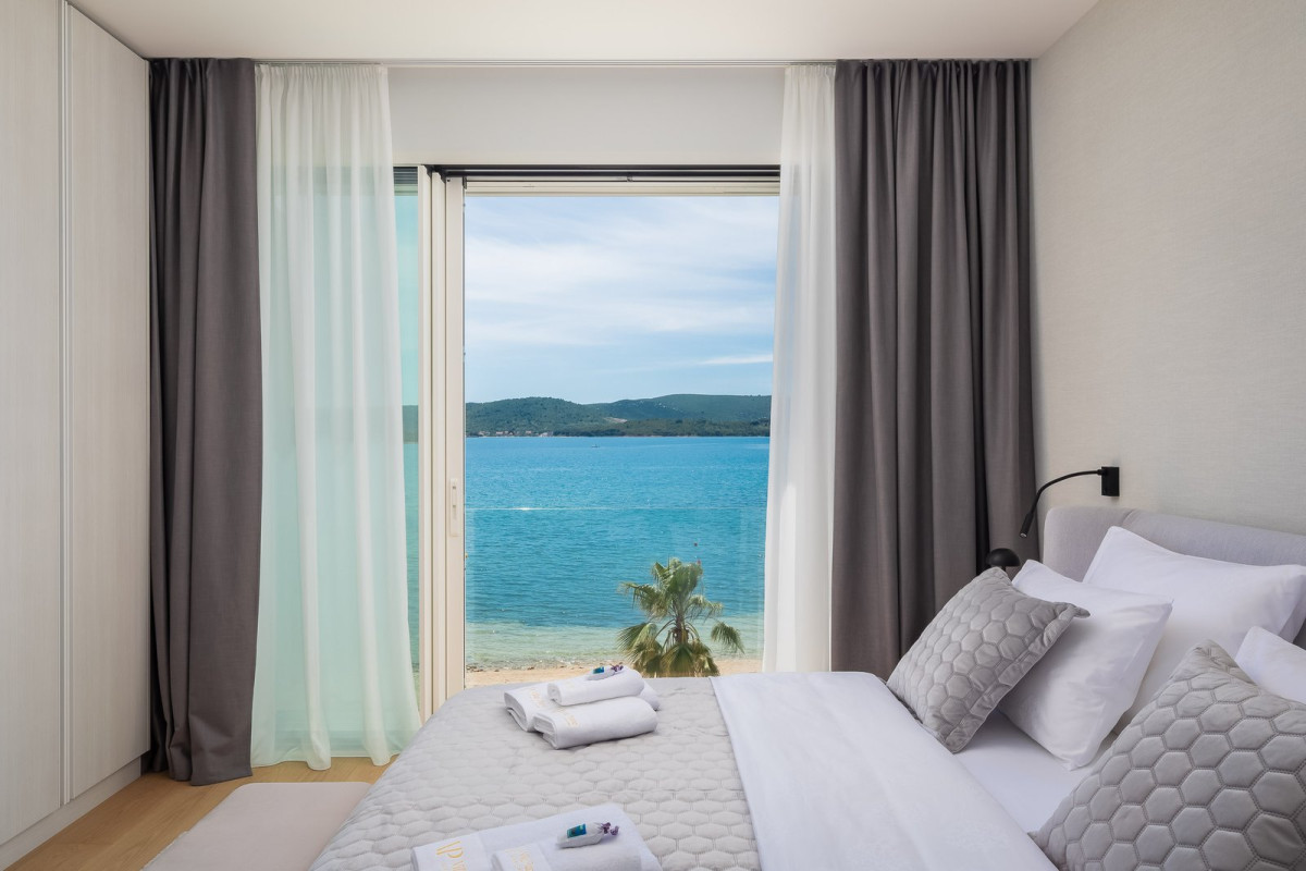 Bright bedroom with a double bed and a floor-to-ceiling window opening onto the sea and beach, Villa Piano Turanj near Zadar